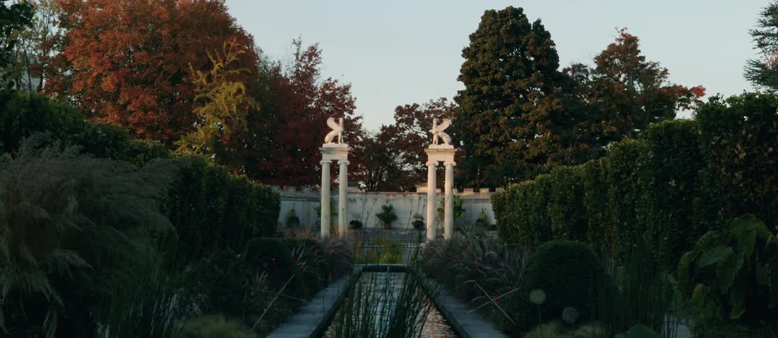 A formal garden with a central water feature and white columns topped with statues