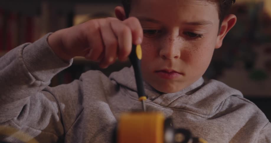 Boy uses a screwdriver while working on a project indoors