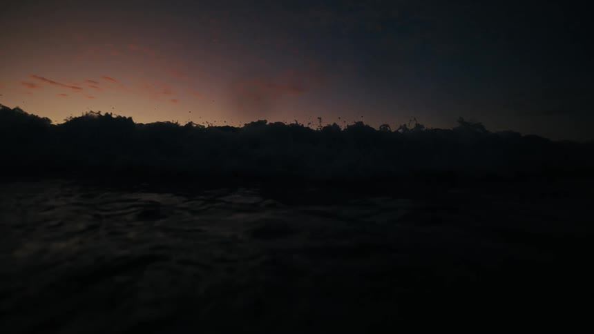 A wave moves along in the ocean at sunset
