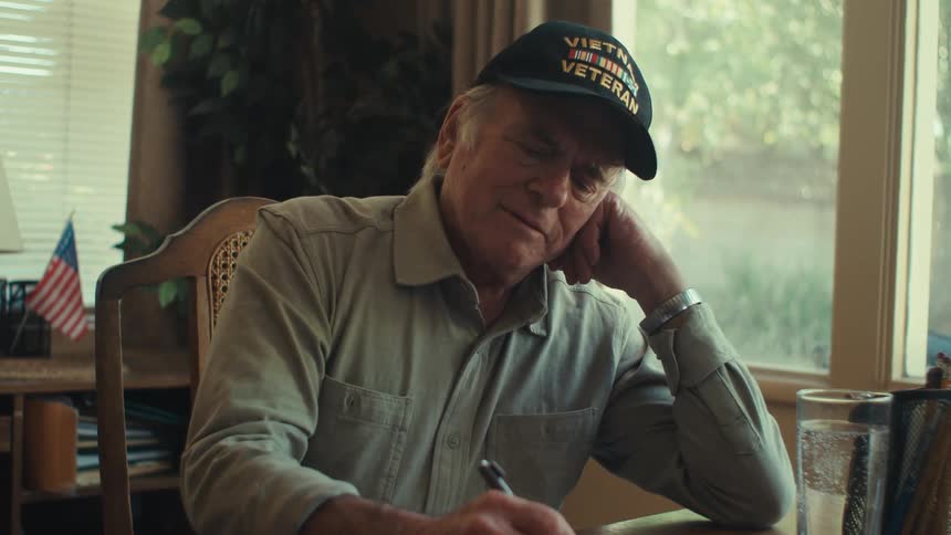 Veteran thinks while writing a letter at a table