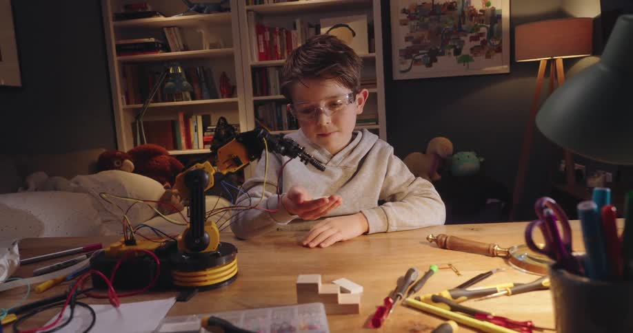 A boy interacts with a small robotic arm placed over a desk at home