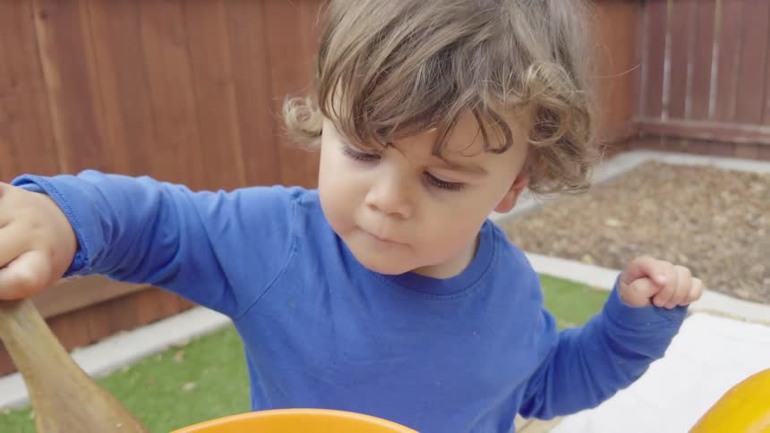 Little boy playing with a slotted spoon in a bucket in the backyard