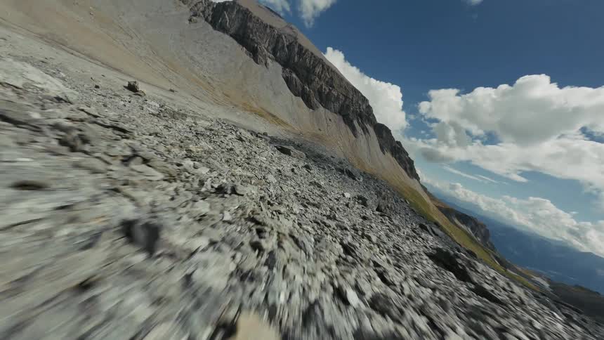 Rocks cover the ground surrounding a pond on a plain near the base of a cliff on a cloudy day