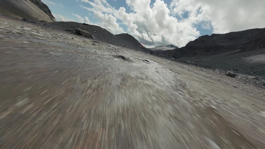 A fast paced ground level shot speeds through a rocky mountain pass revealing a vast dry terrain under a cloudy sky in Switzerland