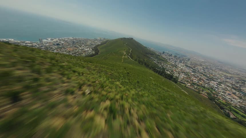 Aerial view of a city from a high mountain point with clear sky above and vegetation and the sea in the background