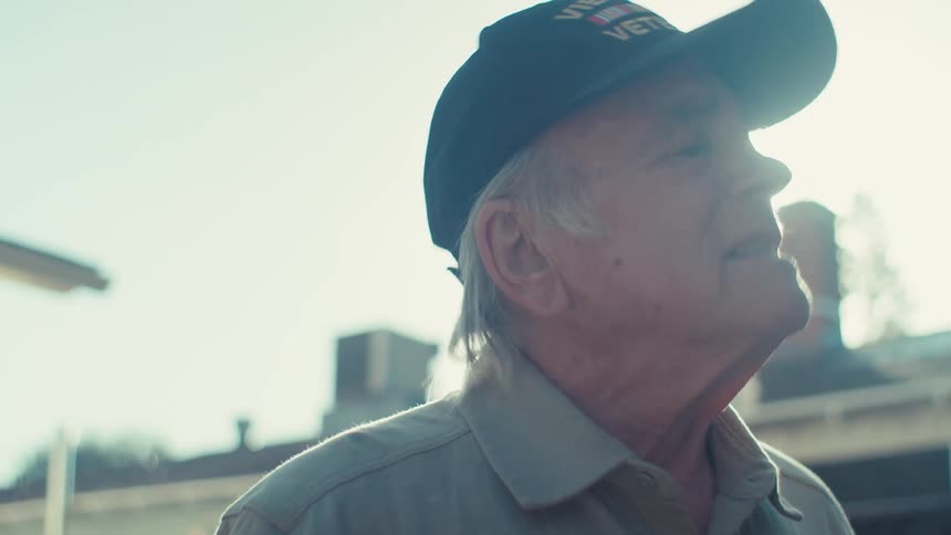 An elderly man in a baseball cap looks upward