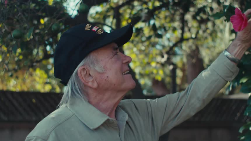 A man smells a flower in his yard