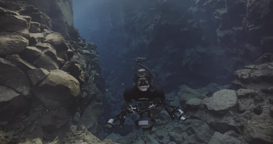 Diver equipped with an underwater camera explores a deep crevice with rocky walls