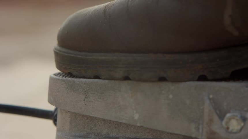 Close up of a booted foot pressing a tool