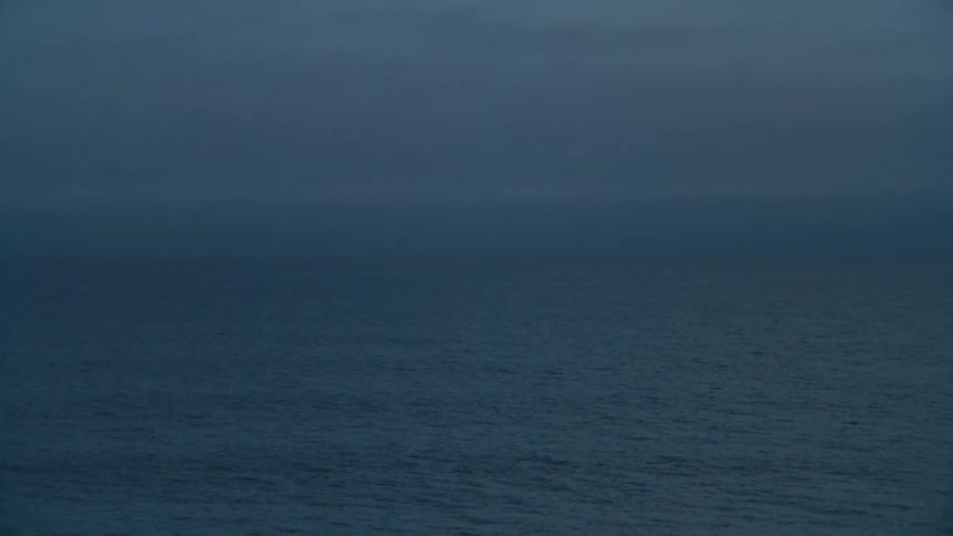 A vast dark ocean stretches out under an overcast sky