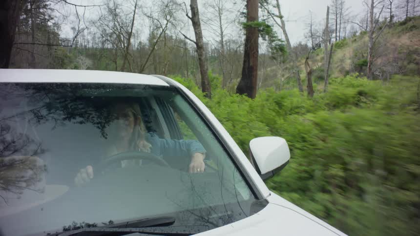 A woman driving a white car on a country road