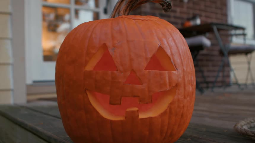 A carved jackolantern sits on a porch lit from within