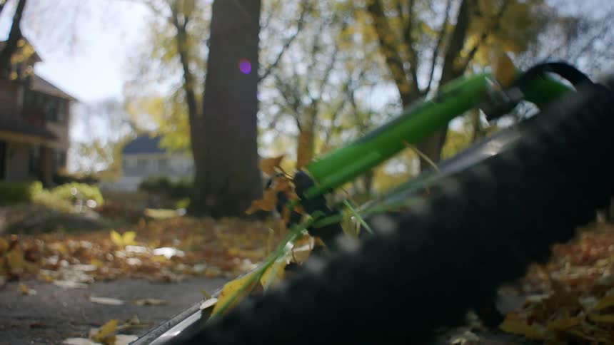 A child picks up a bicycle from the ground in a neighborhood covered in autumn leaves