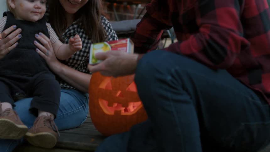 A family light up a jack o lantern on the porch at dusk
