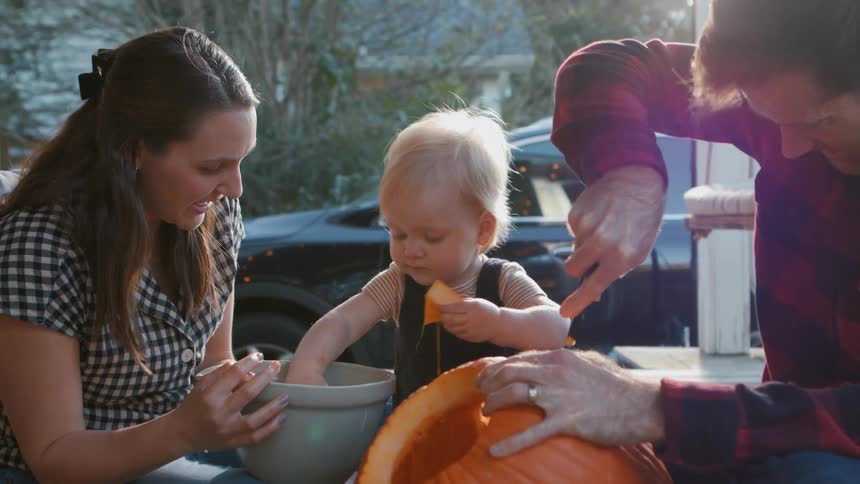 A family carving a jack o lantern on the porch at dusk