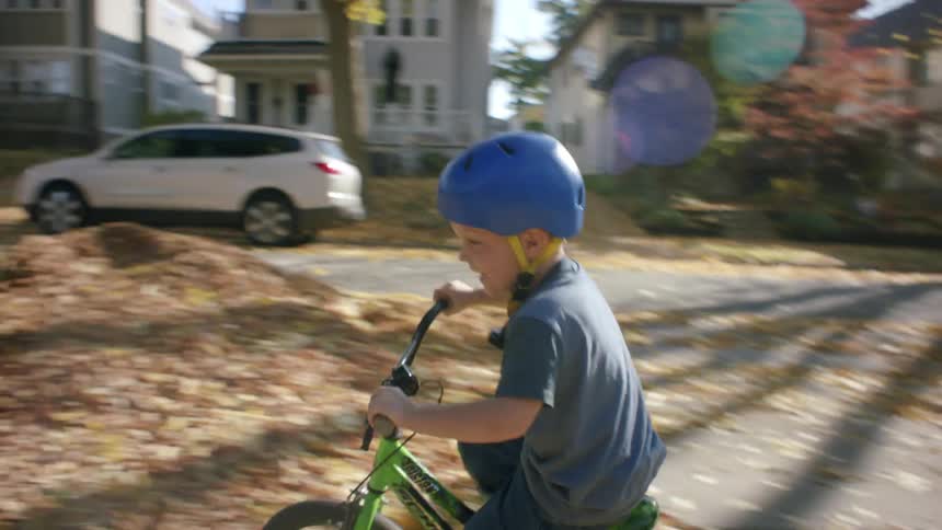 A child wearing a helmet rides a bicycle in the neighborhood during fall