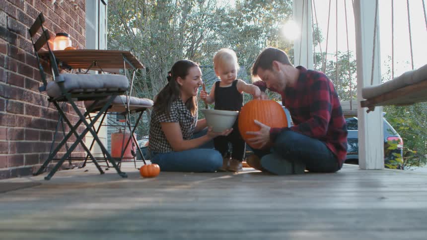 A family carving a jack o lantern on the porch at dusk