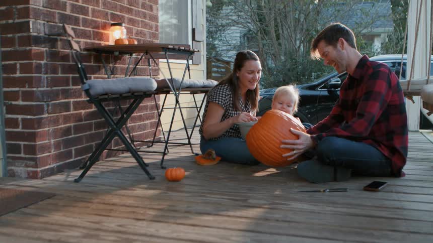 Family sitting outside their home with the father holding a halloween pumpkin and interacting with his young son