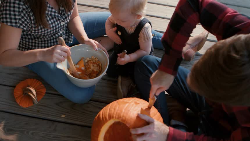 A family carves pumpkins together on a porch for halloween