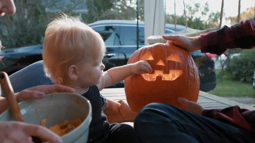 Little boy next to his parents interacting with a halloween pumpkin
