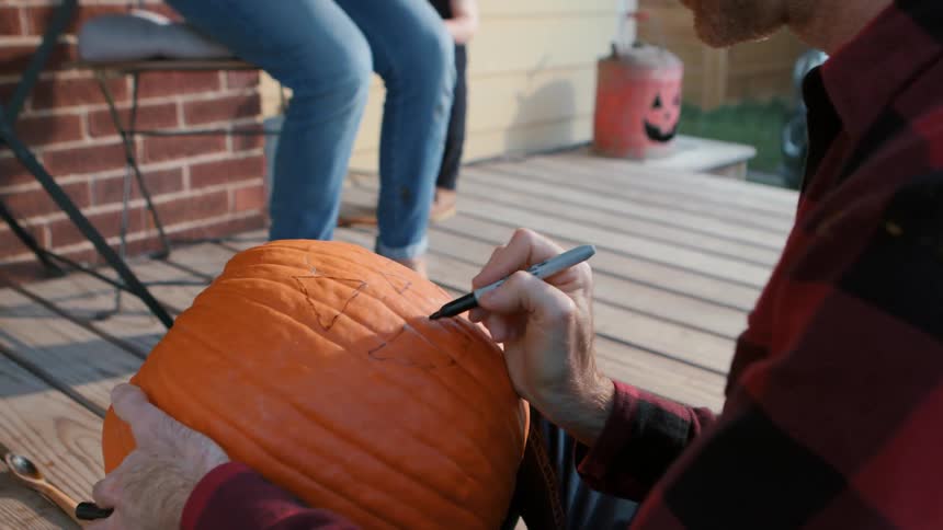 A family carving a jack o lantern on the porch at dusk