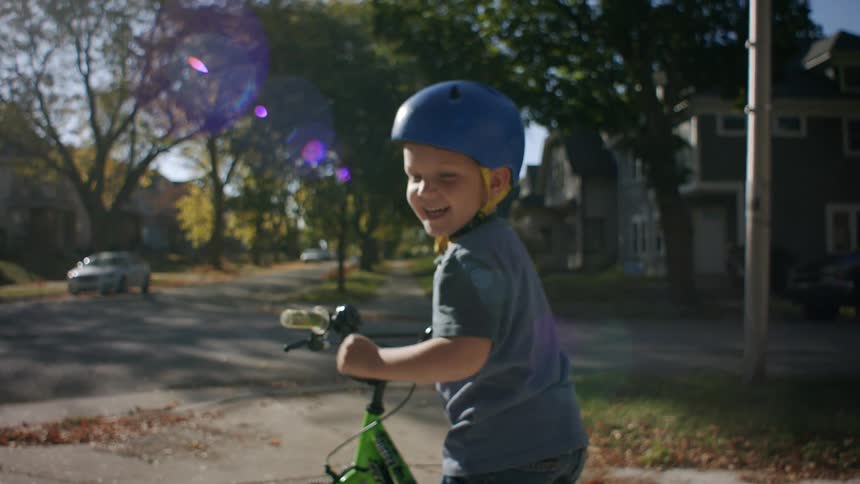 A happy child rides a green bicycle in the neighborhood reaching for the camera