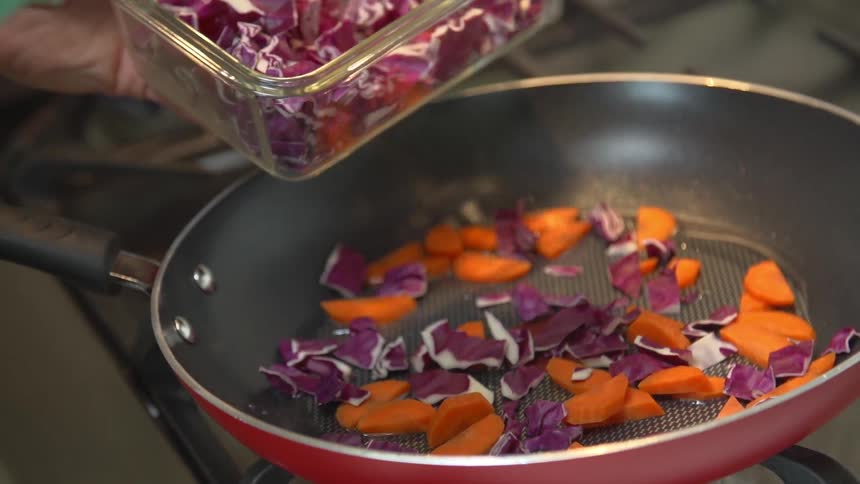 Someone adding chopped red cabbage to a frying pan