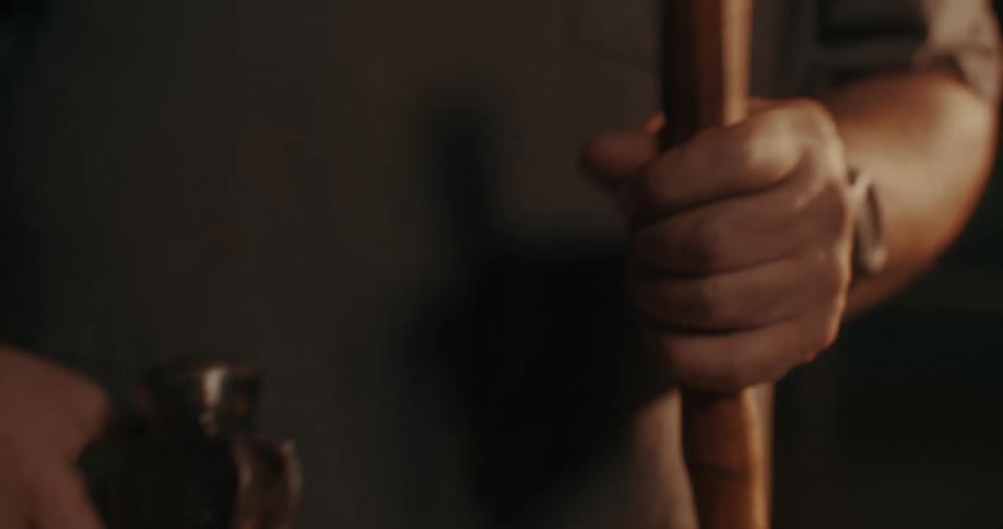 A man fits a new hammer head onto a wooden handle in a dimly lit workshop