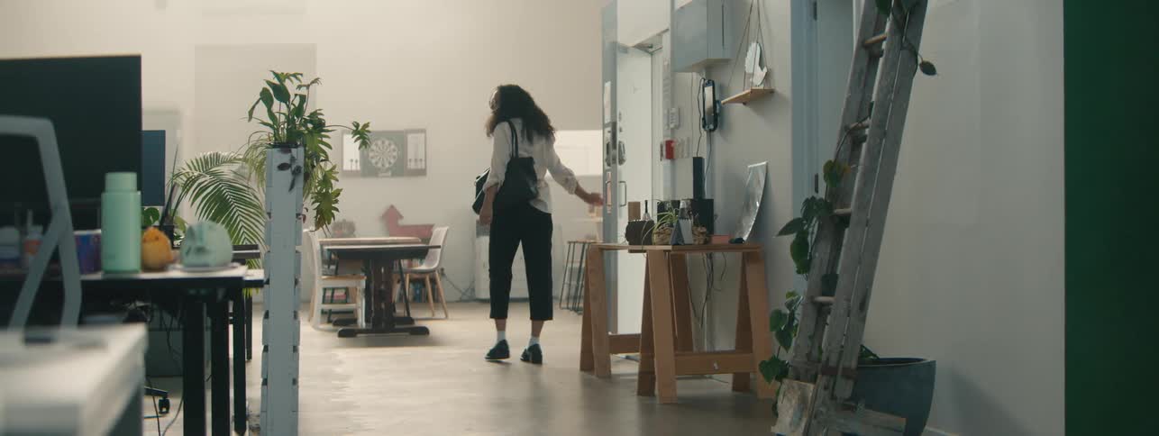 A young woman with curly hair walks through a modern office