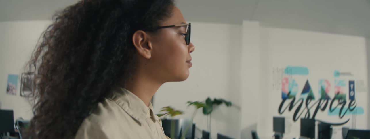 A young woman with curly hair walks through a modern office