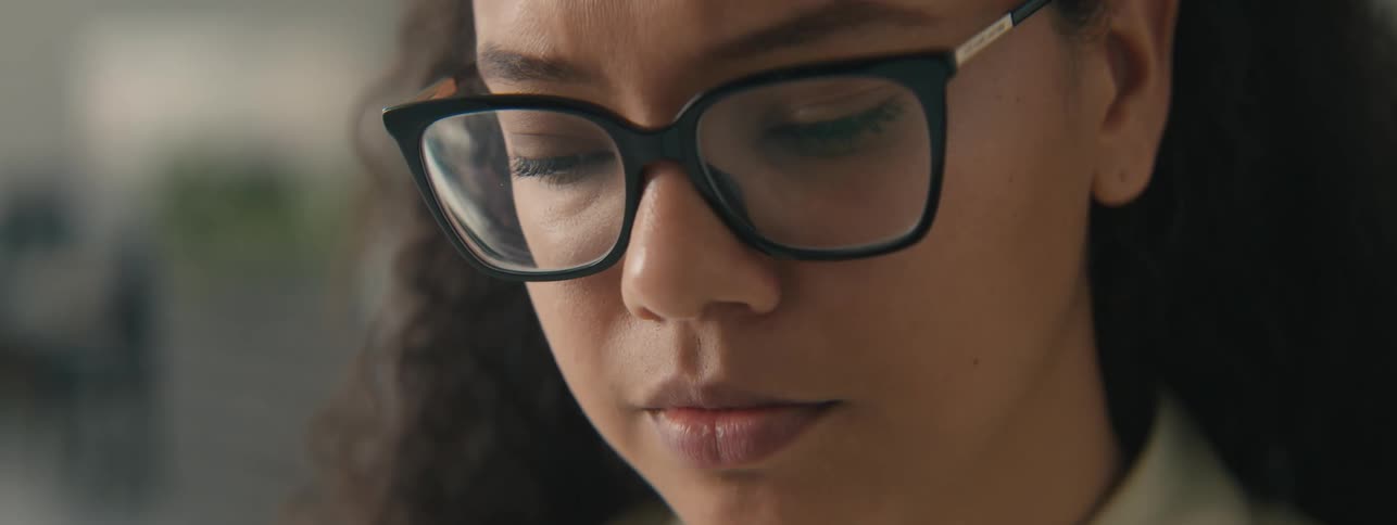 Closeup of the face of a young woman with curly hair and glasses focused on a task