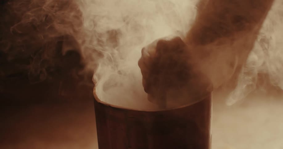 A hand stirs a metal rod in a pot of steaming liquid