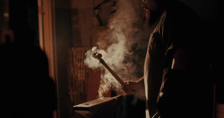 Man placing a wooden handle on hot metal and forming a hammer