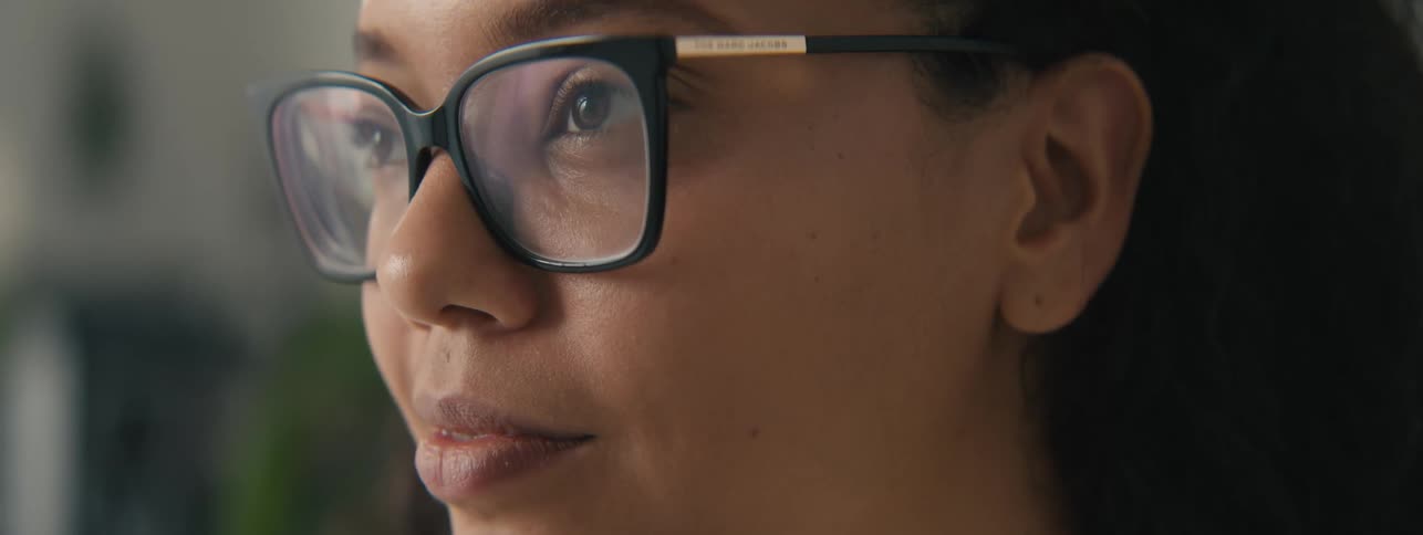 Closeup of the face of a young woman with curly hair and glasses focused on a task