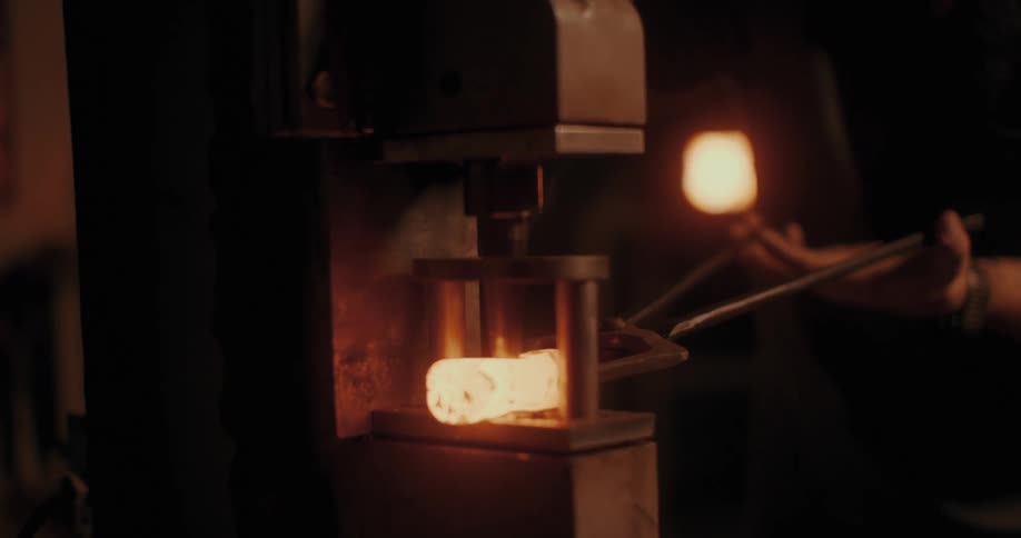 A blacksmith uses tongs to hold a redhot piece of metal being worked on by a machine