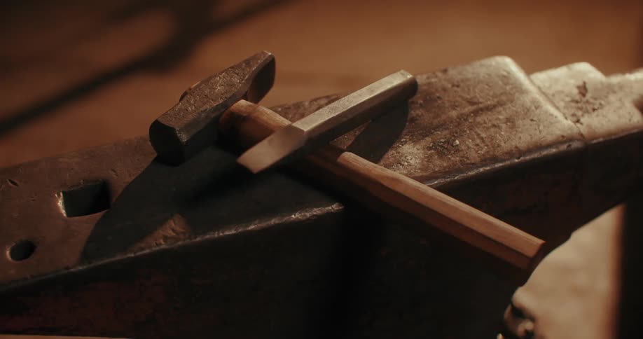 A hand placing a hammer and chisel over an anvil