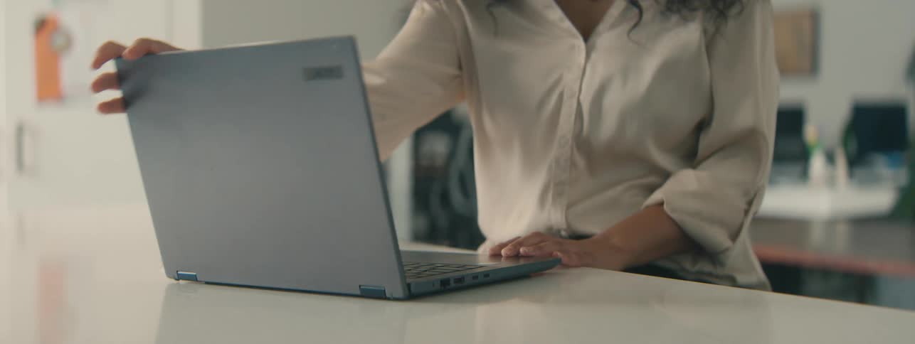 A young woman with curly hair and glasses sits in the office to work on her laptop