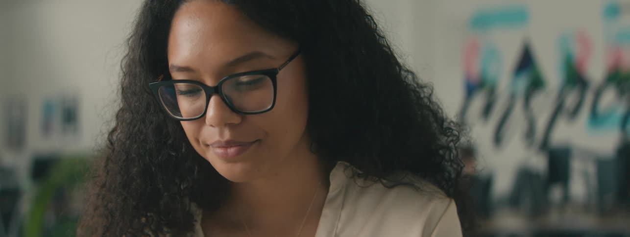 Portrait of a curlyhaired woman wearing glasses and looking focused indoors