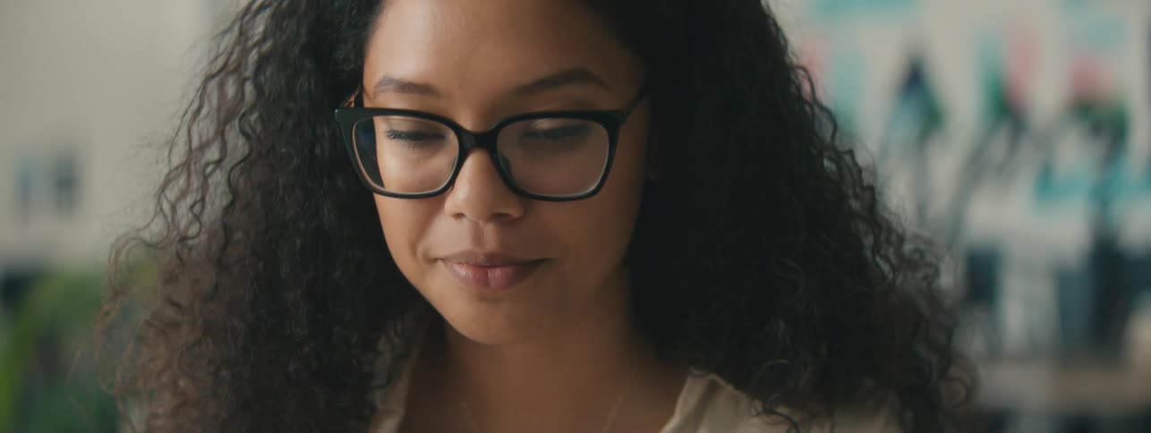 Closeup of the face of a young woman with curly hair and glasses focused on a task
