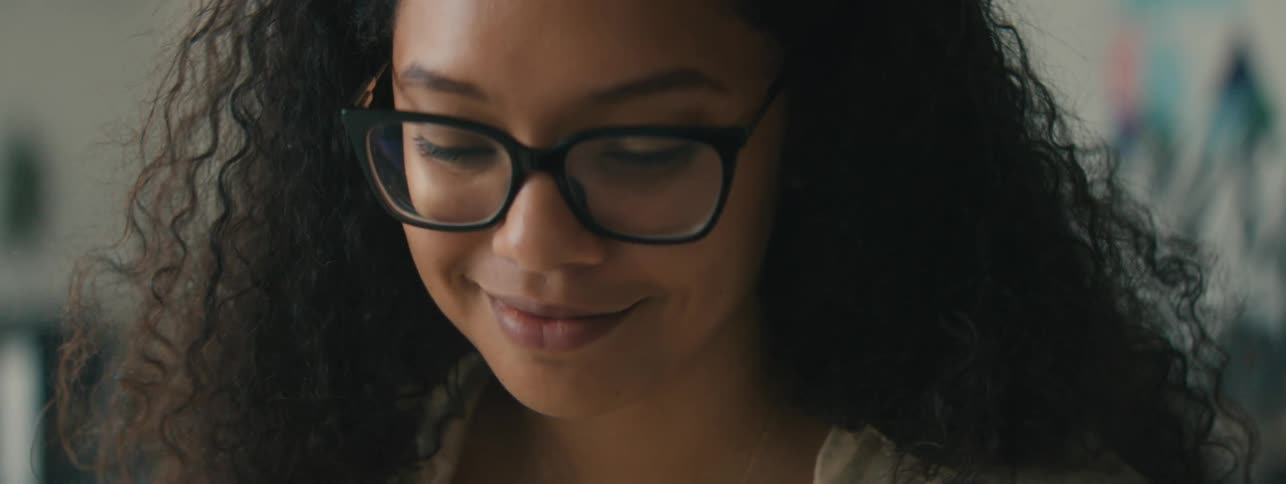 Closeup of the face of a young woman with curly hair and glasses focused on a task
