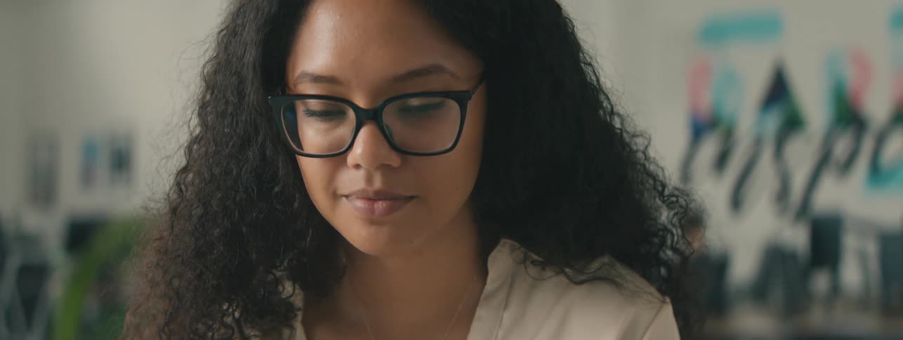 Closeup of the face of a young woman with curly hair and glasses focused on a task