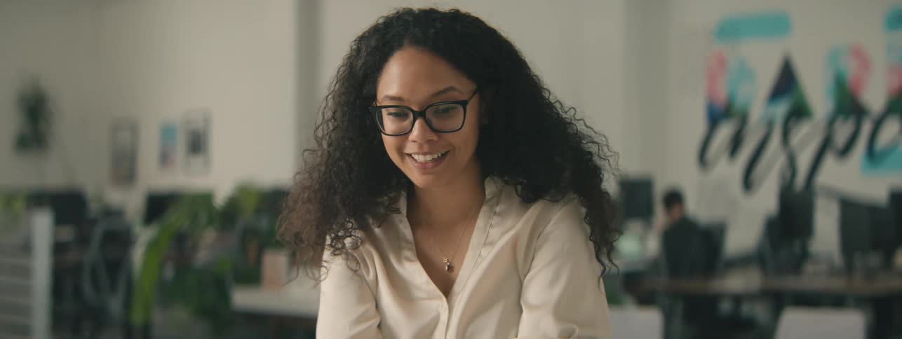 A happy woman with curly hair gestures while talking on a video call in the office
