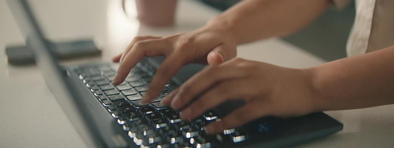 A pair of hands diligently types on a laptop keyboard focused on the task at hand