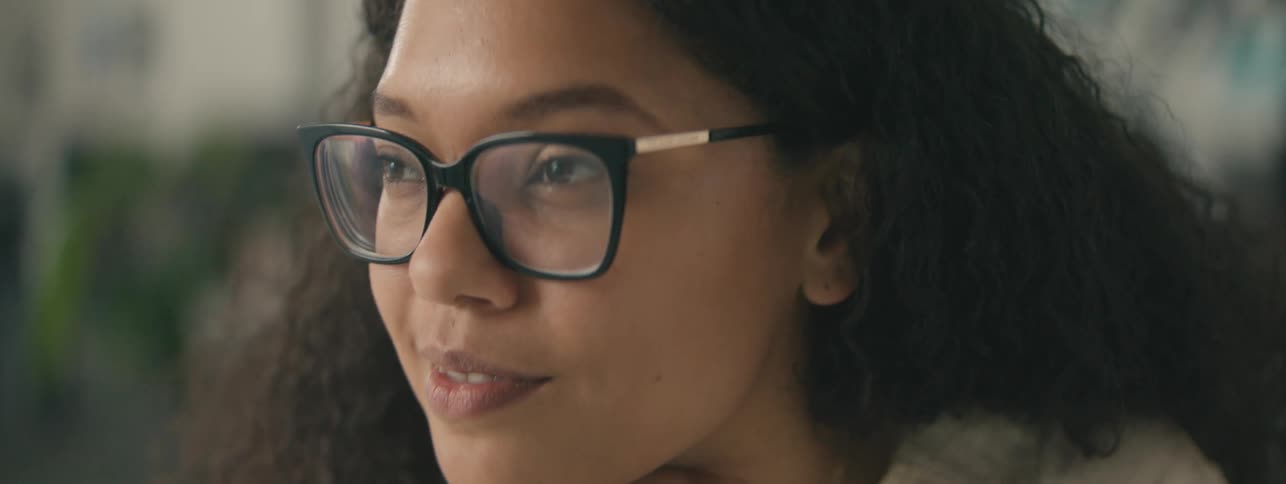 Closeup of the face of a young woman with curly hair and glasses