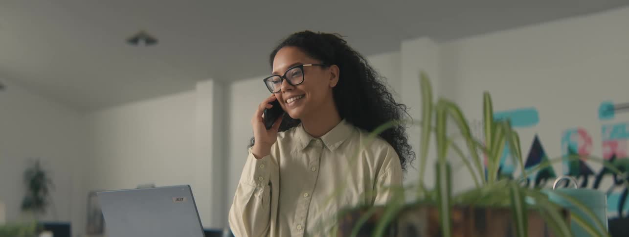 A happy woman with curly hair talking on a smartphone in the office