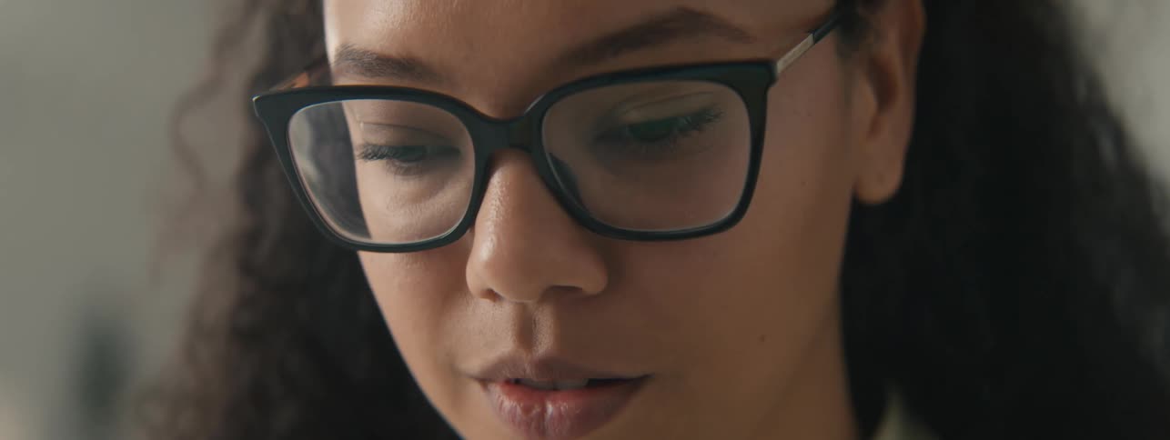 Closeup of the face of a young woman with curly hair and glasses focused on a task