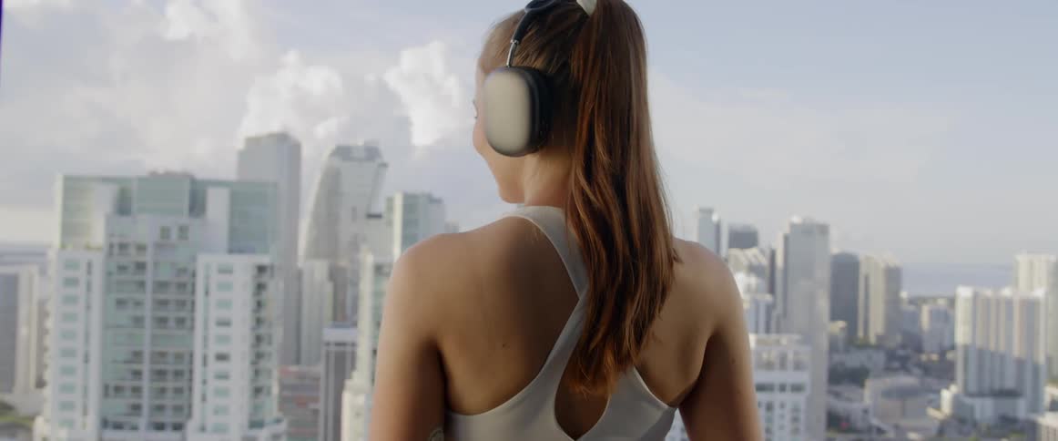A woman wearing headphones looks at the city skyline from large windows