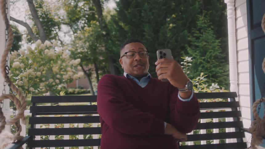 A man sitting on a hanging chair in the porch talking on the phone