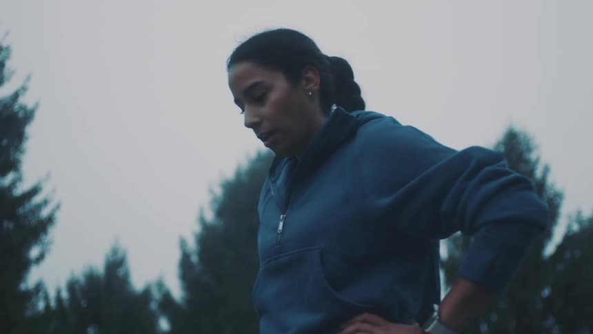 A woman in a blue sweater catches her breath after jogging
