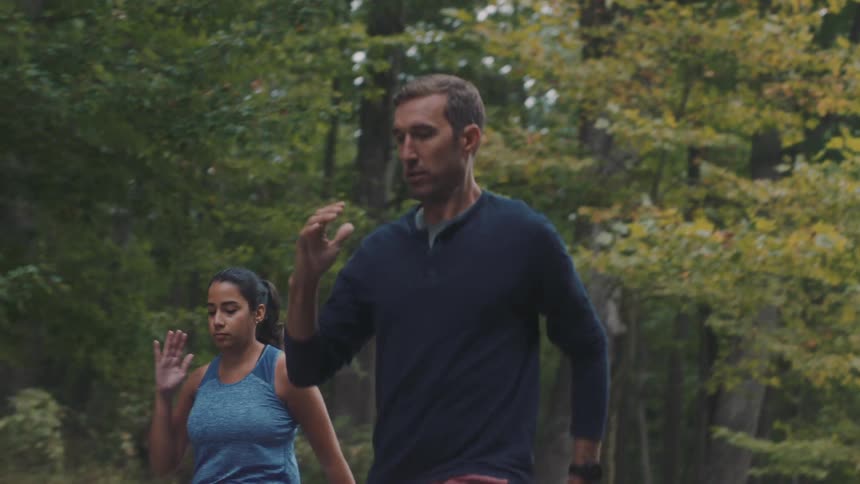 A male trainer teaches a woman how to do walking lunges on an autumn day